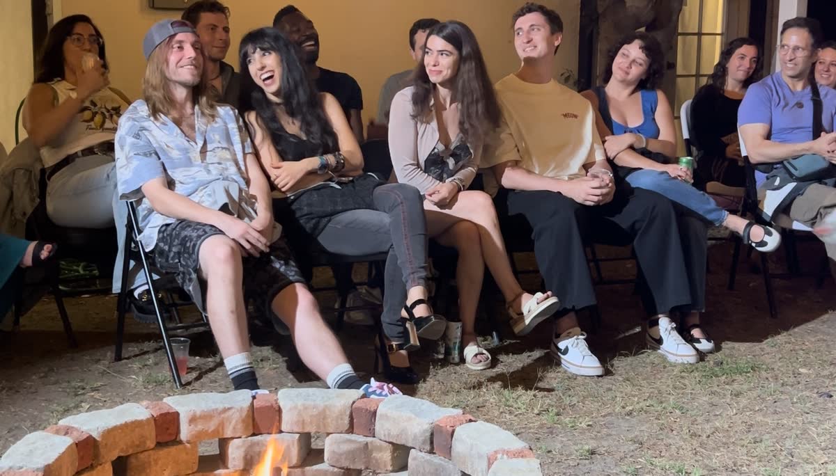 The front row seen across the brick firepit, a dozen people packed shoulder to shoulder and laughing at the same moment.